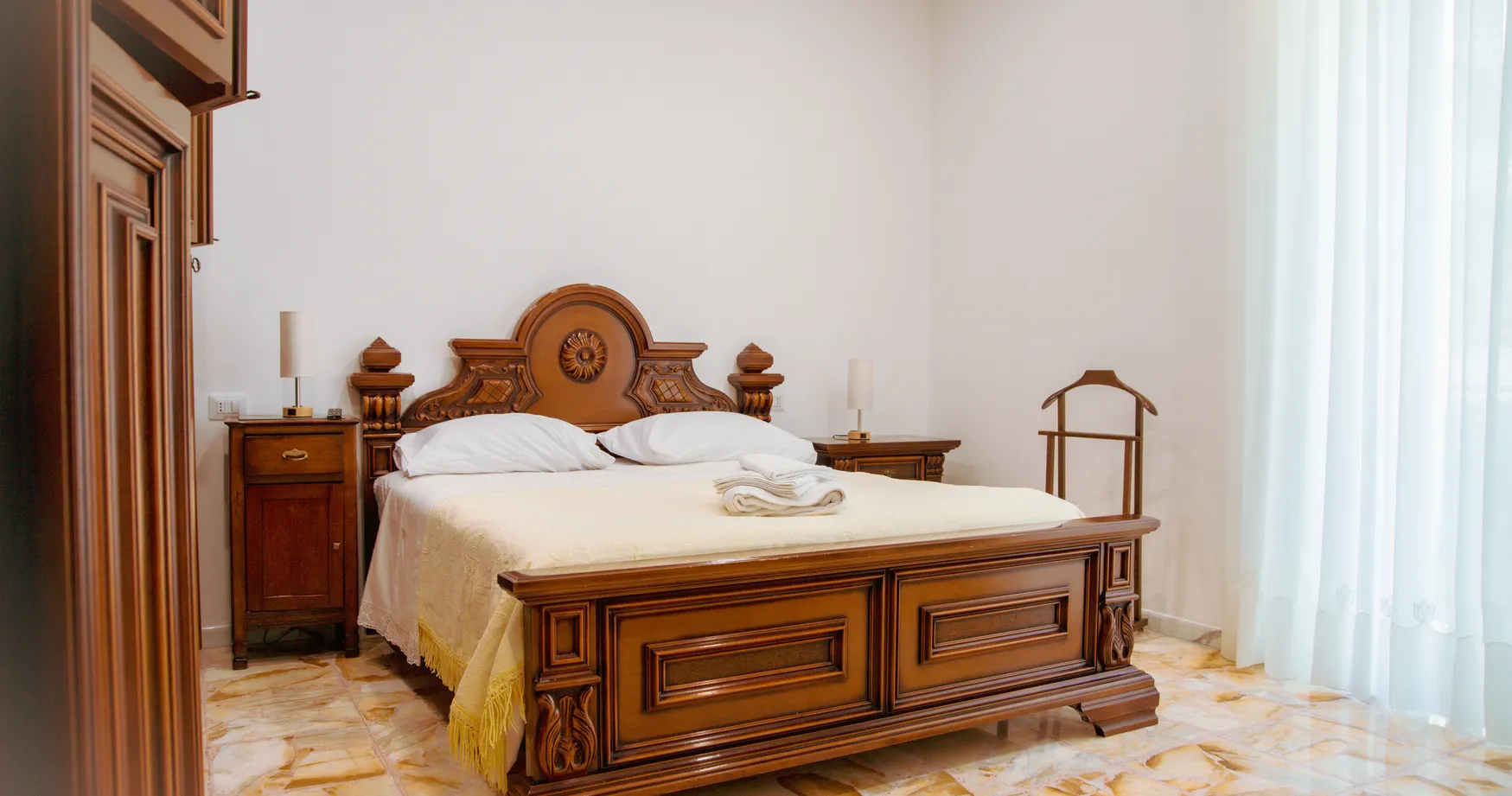 Camera Maria: Il letto matrimoniale in noce intagliato, l’armadio antico e il pavimento alla palladiana.